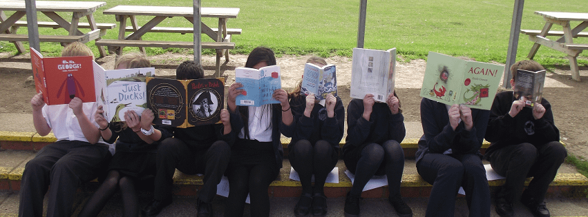 8 children sitting in a row on school steps, all reading with books held up to cover their faces